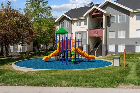 A playground with a yellow slide in front of a building.