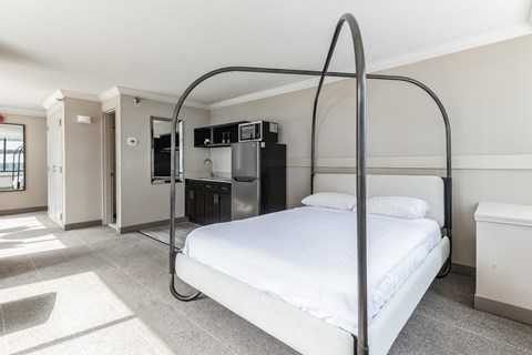 A white bed with a metal frame in a room with a kitchen area in the background.
