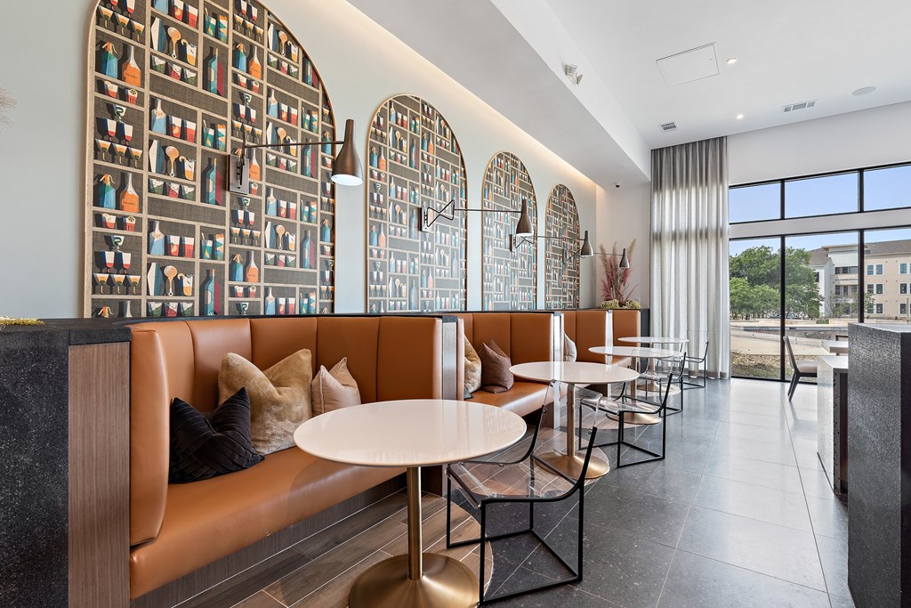 A modern restaurant with a long table and chairs, a large window with a view of buildings outside, and a wall with a pattern of bottles.