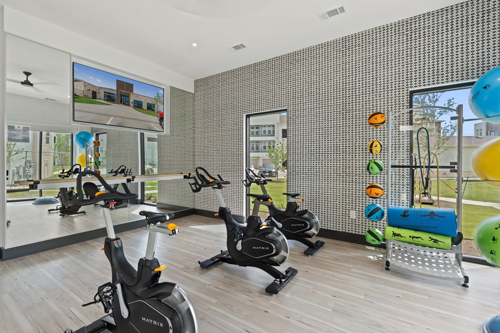 A gym with exercise bikes and a TV screen showing a building.
