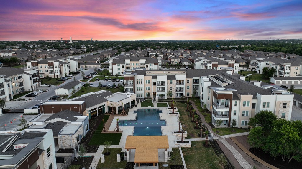 A sunset view of a residential area with apartment buildings and a pool.