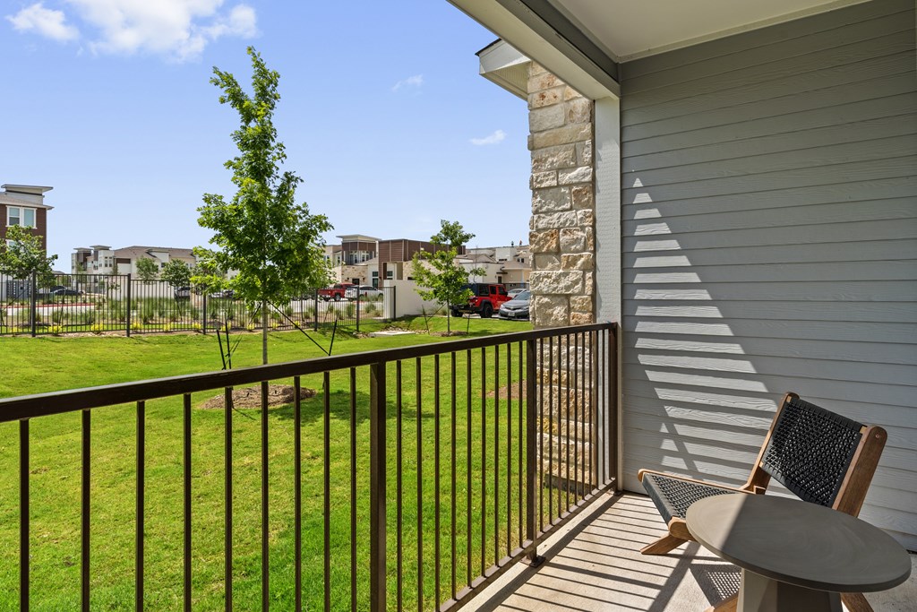 A balcony with a table and chairs overlooks a grassy area and buildings.