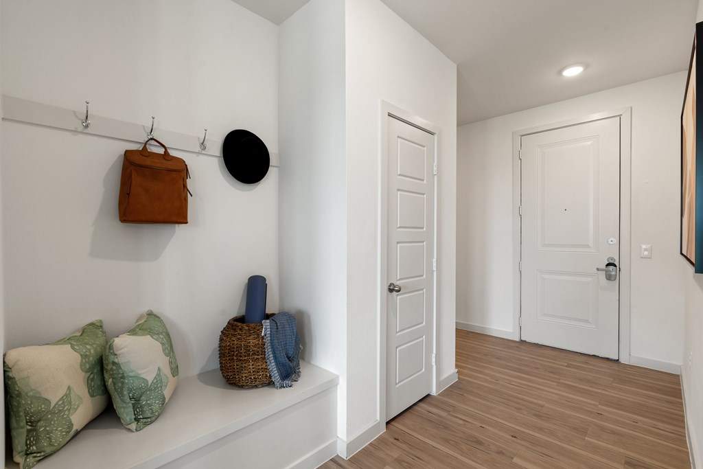 A hallway with a bench and a bag hanging on the wall.