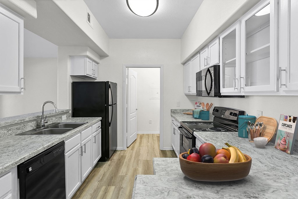 a kitchen with white cabinets and black appliances and a bowl of fruit