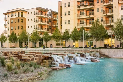 a city with a waterfall in front of some buildings at Discovery at The Realm, Lewisville