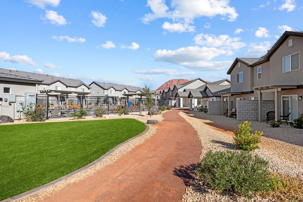 a pathway leading to a row of houses with a field of green grass and