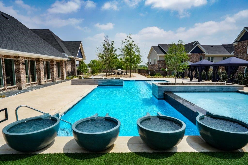 A swimming pool with four bowl-shaped hot tubs lined up on the grass.