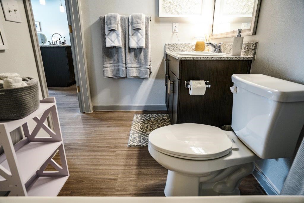 A white toilet sits in a bathroom with a wooden floor and a white sink.