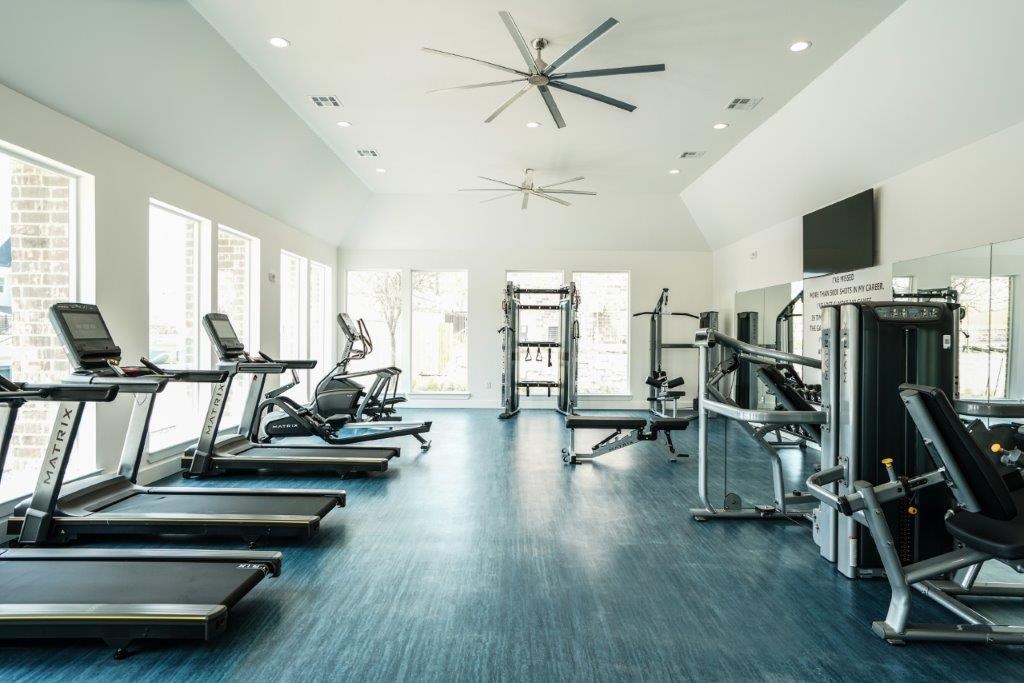 A spacious gym with treadmills, exercise machines, and a ceiling fan.