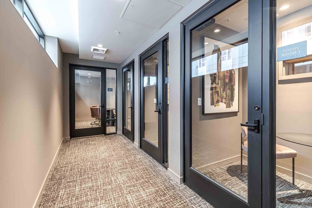 A hallway with a carpeted floor and glass doors leading to a room with a sign that says "FOCUS ROOM".