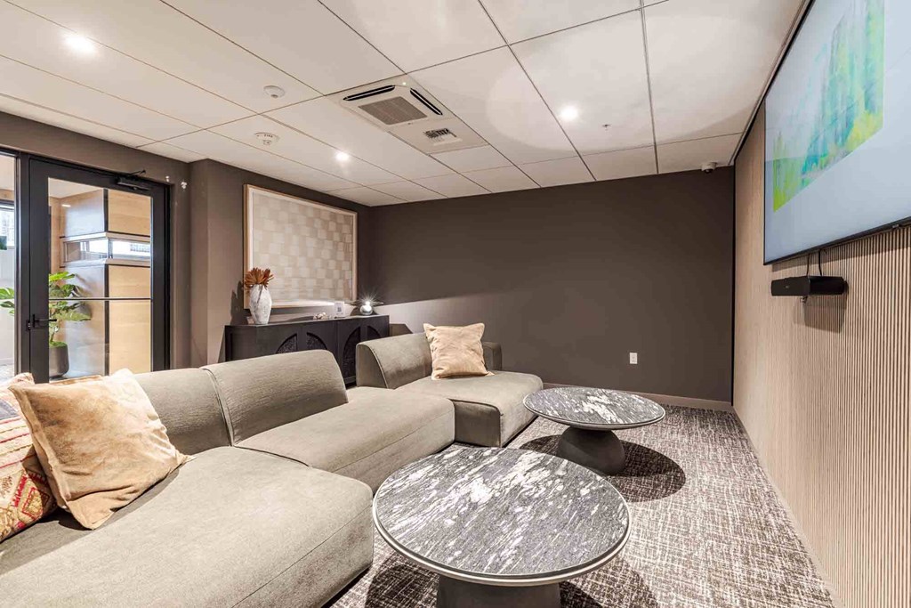 A modern living room with a grey sofa, a glass coffee table, and a flat screen TV mounted on the wall.