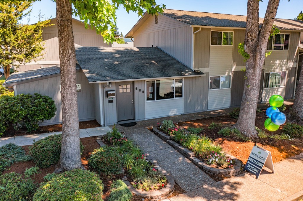 the front of the house with two trees and a sign in the front yard
