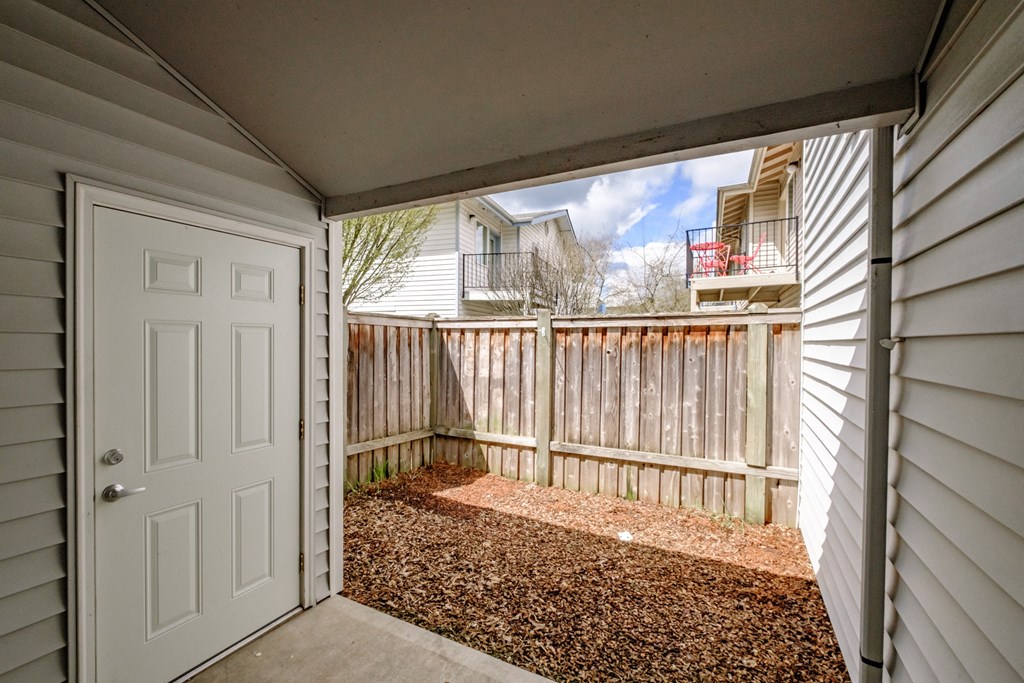 a white door opens to a small patio with a wooden fence