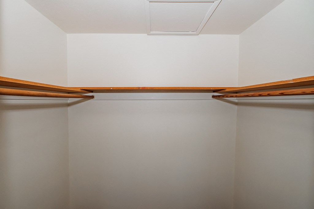 a walk in closet with white walls and wooden shelves