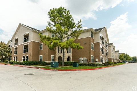 an apartment building with a parking lot and a tree in front