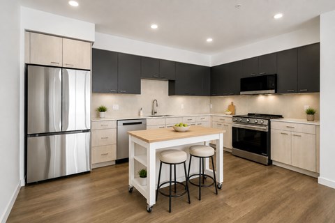 A modern kitchen with a stainless steel refrigerator, black cabinets, and a wooden island.