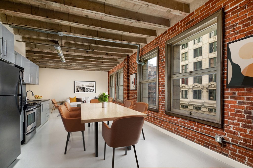 a dining area with a wooden table and chairs in front of a brick wall with large windows