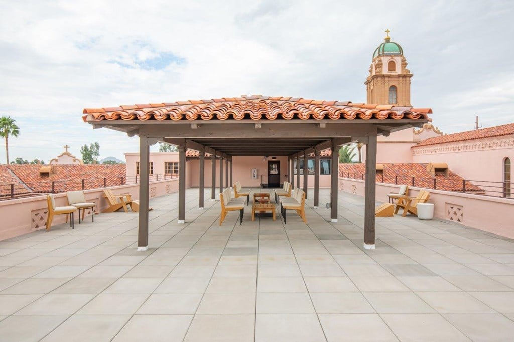 A patio with a roof and chairs is in front of a building with a green dome.