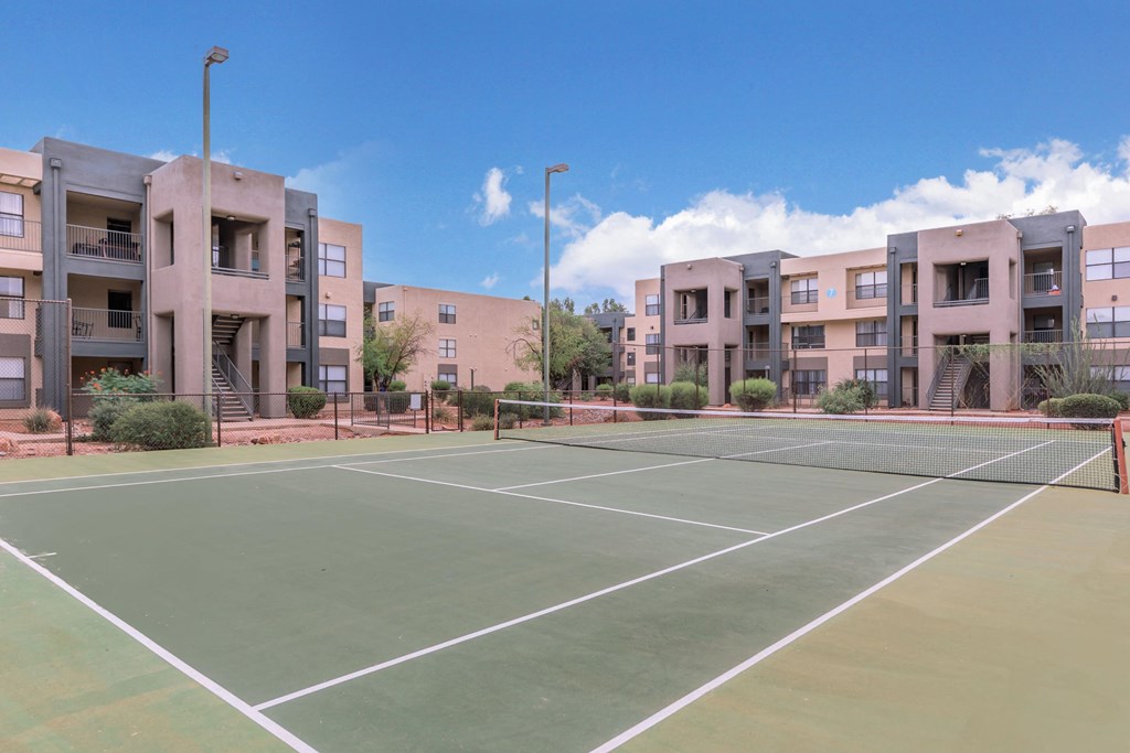 A tennis court is surrounded by apartment buildings.