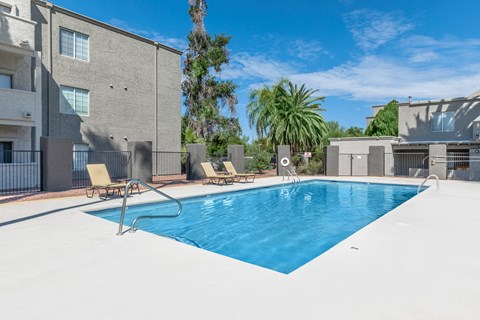 A swimming pool surrounded by lounge chairs and buildings.