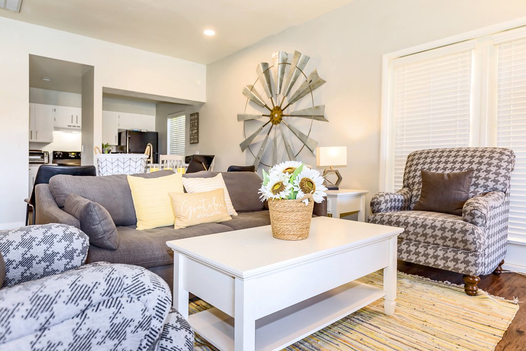 A living room with a grey couch, a white coffee table, and a sunburst mirror.