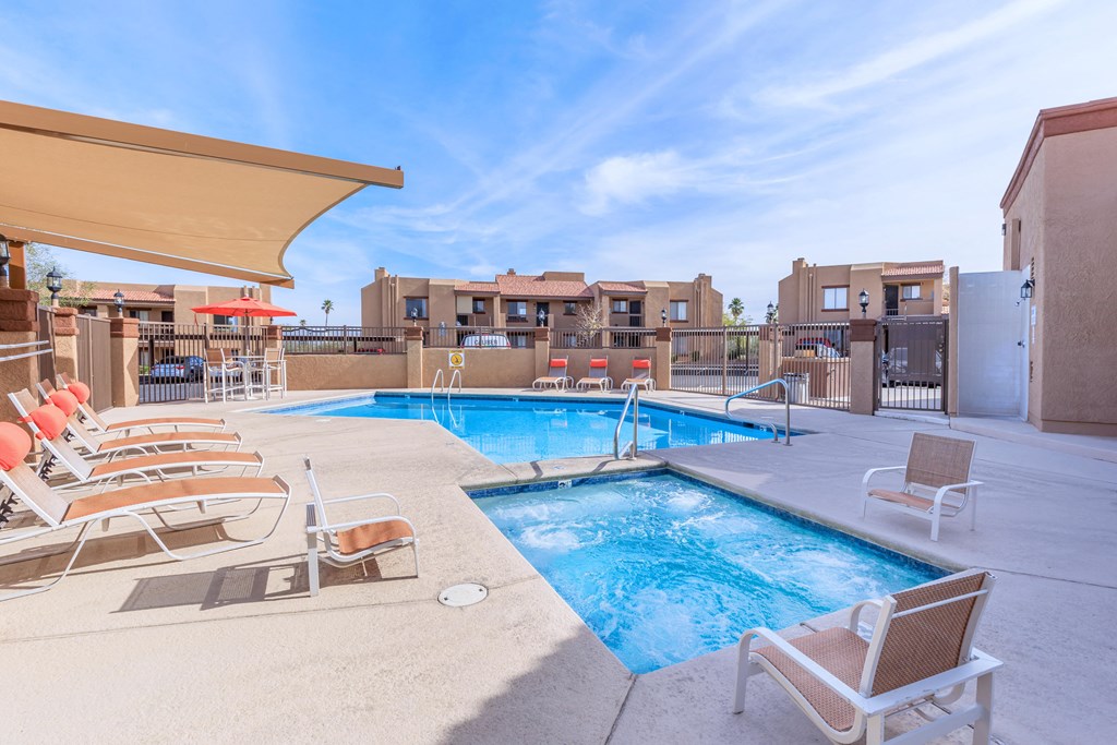 A pool with chairs and a sunshade is surrounded by buildings.