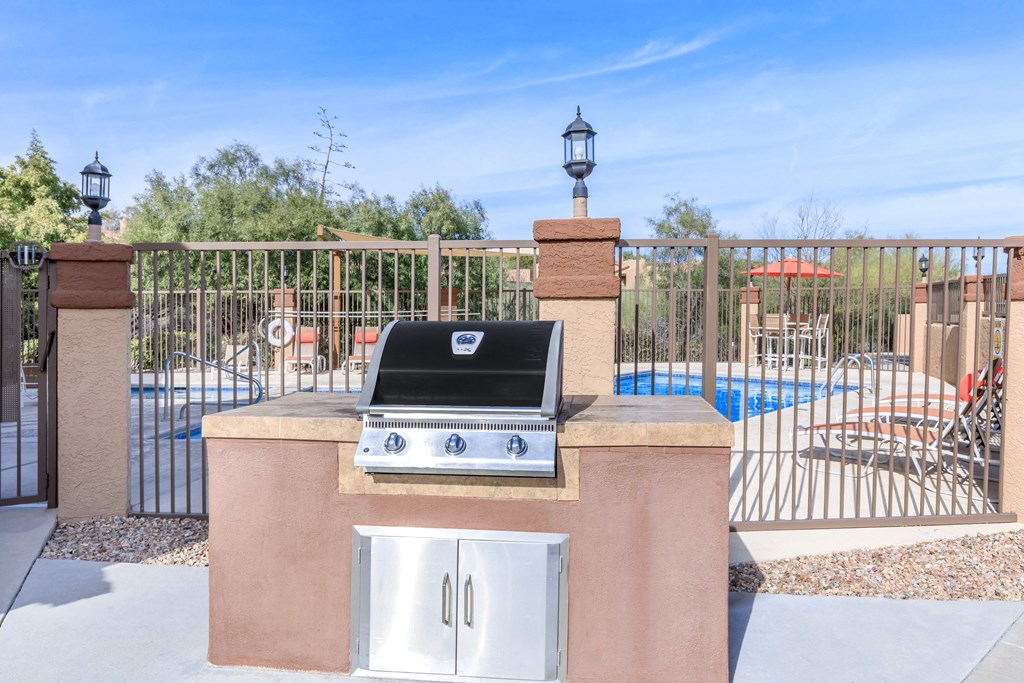 A BBQ grill is on a stand next to a pool.