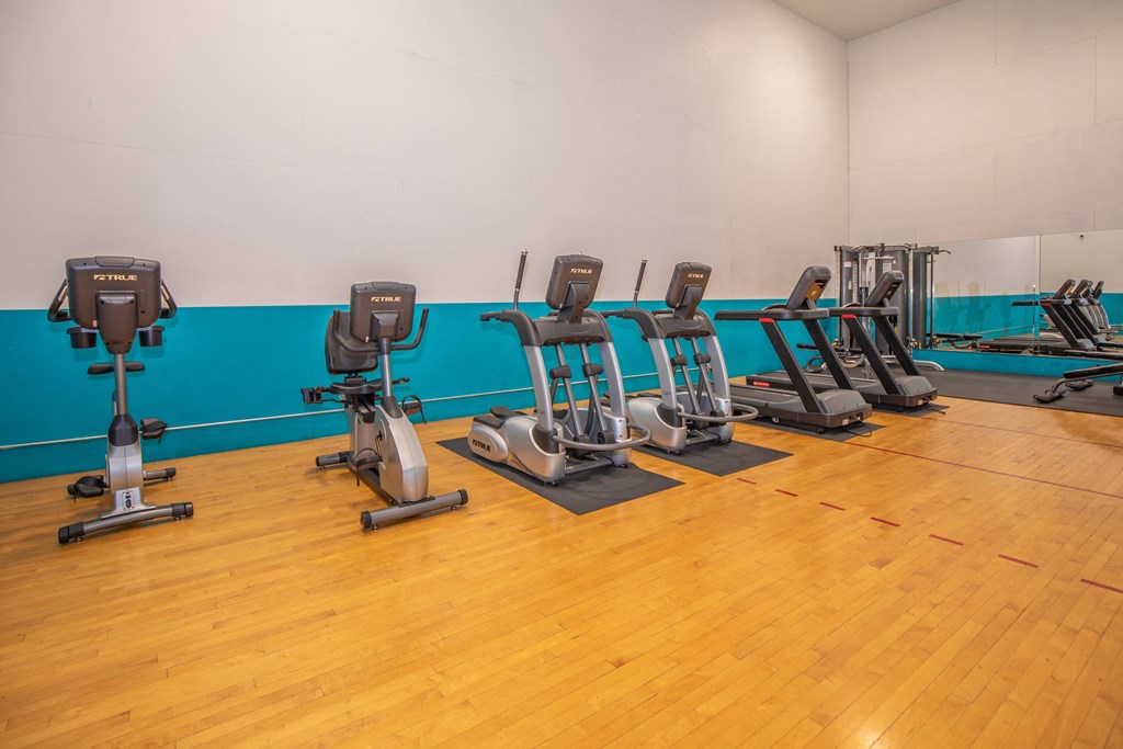 A gym with exercise equipment and wooden floors.