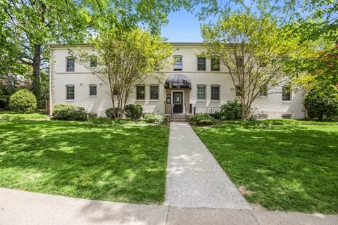 A white house with a black door and windows surrounded by green grass and trees.