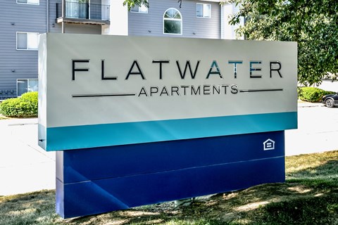 A sign for Flatwater Apartments is displayed in front of a building.