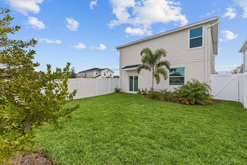 A white house with a green lawn and a tree in front.