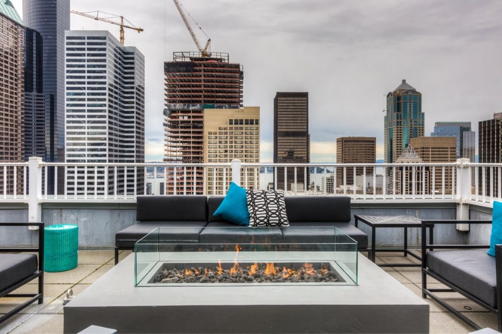 A modern outdoor seating area with a fireplace and a view of a city skyline.