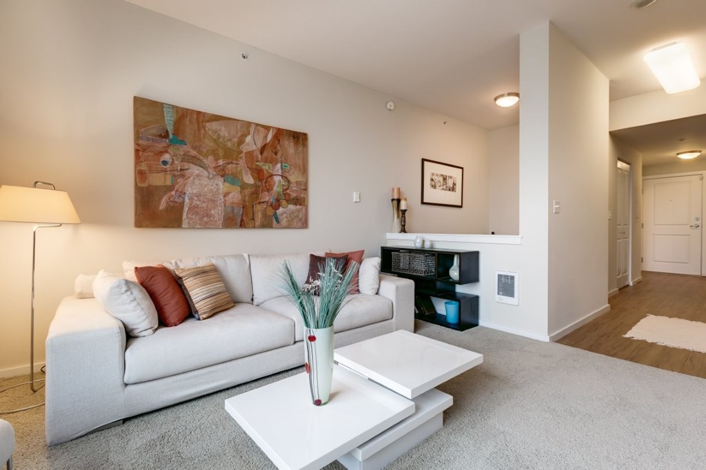 A living room with a white couch and a painting on the wall.