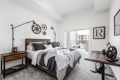 A bedroom with a large bed, a wooden table, and a window with a view of a building outside.