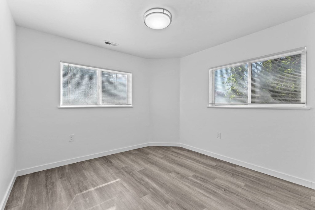 an empty room with wood flooring and two windows