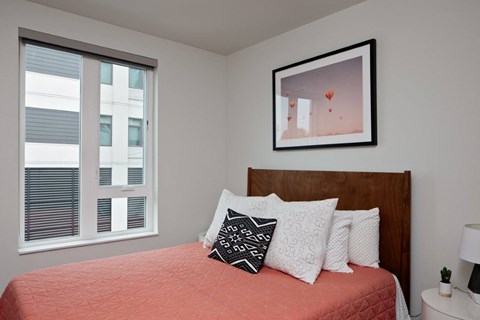 A bedroom with a red bedspread and a framed picture on the wall.