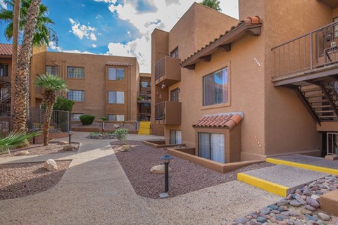A courtyard with a building in the background and a palm tree to the left.