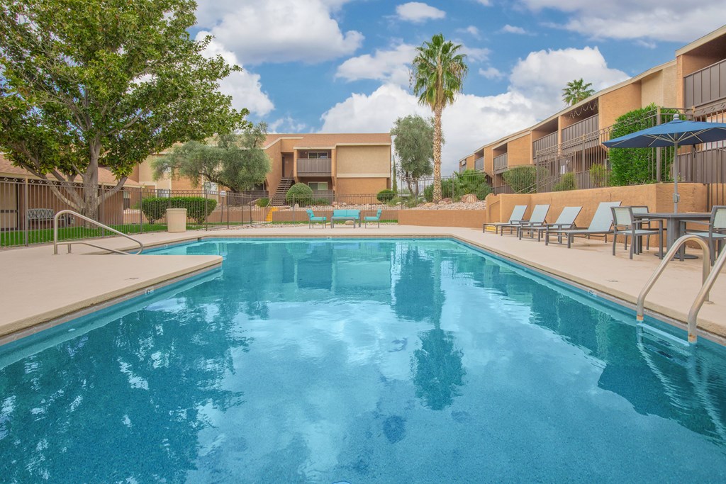 A swimming pool surrounded by lounge chairs and palm trees.