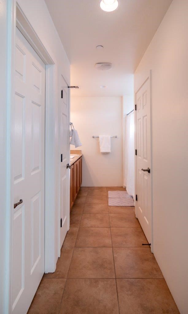 A hallway with white doors and brown tile flooring.