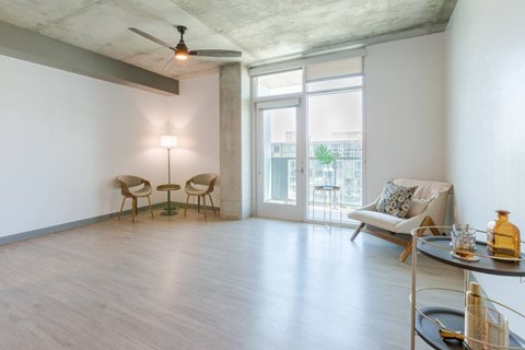 A living room with a ceiling fan, two chairs, a sofa, and a table with a bottle on it.
