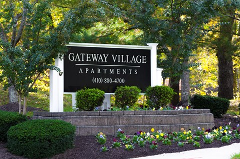 A sign for Gateway Village Apartments is displayed in front of some trees.