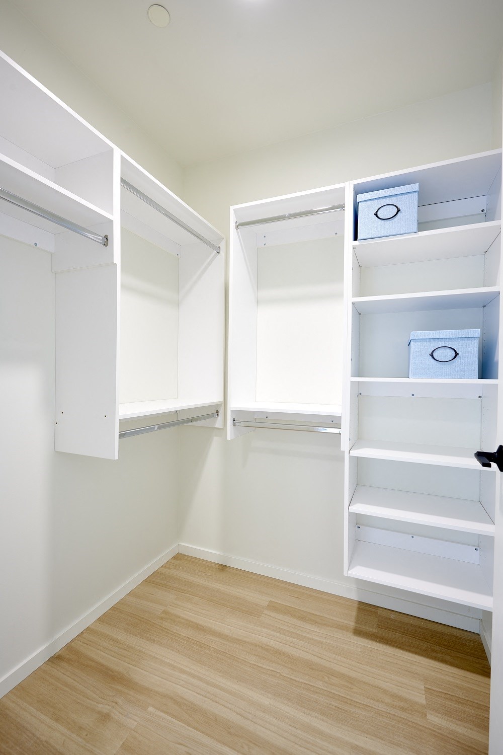 a walk in closet with white shelves and a wood floor