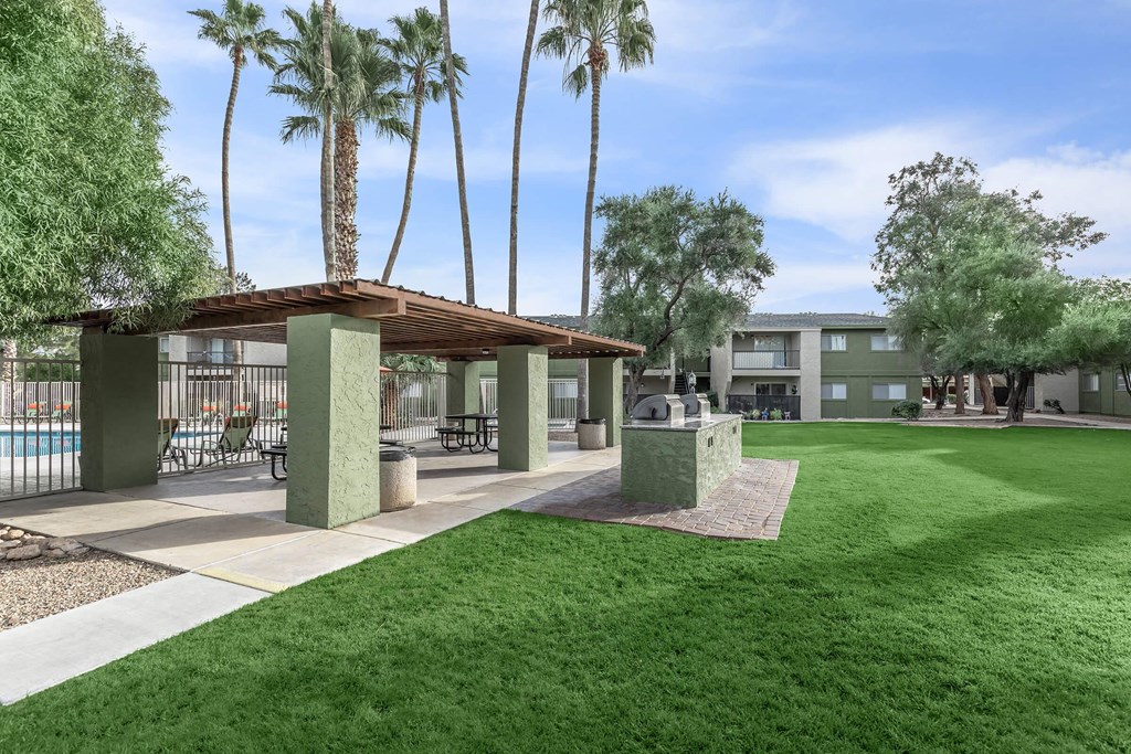A sunny day at the poolside with palm trees and a covered seating area.