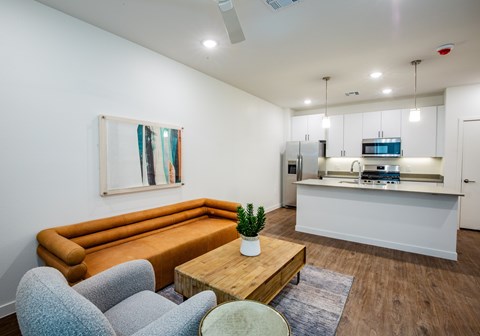 A living room with a brown sofa, grey chairs, a wooden coffee table, and a painting on the wall.