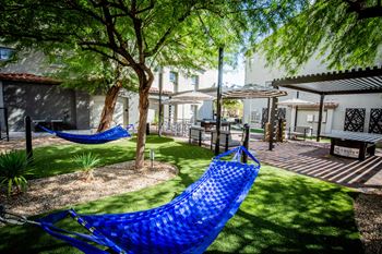 A blue hammock is strung between two trees in a courtyard.