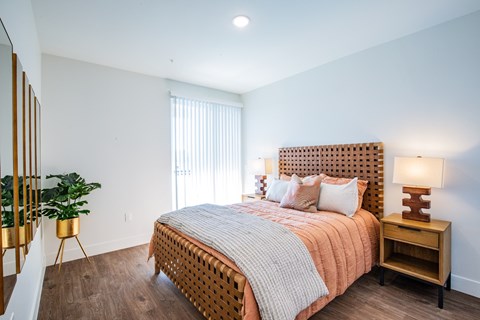 A bedroom with a bed, nightstand, and a potted plant.