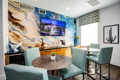 A living room with a table and chairs and a TV on the wall.