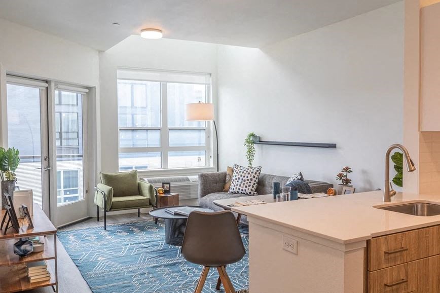 A modern kitchen and living room are connected by a glass door.