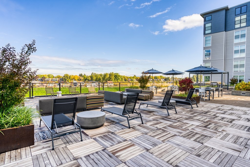 A patio with black chairs and tables is surrounded by a tall building.