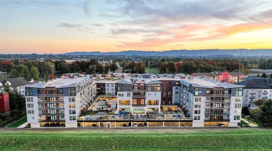 A large, modern apartment complex with a green field in the foreground and a cityscape in the background.